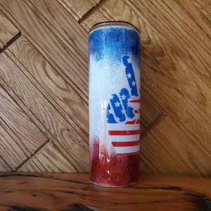 May include: A red, white, and blue glitter tumbler with a peace sign design. The peace sign is made up of the American flag.