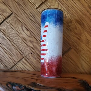 May include: A red, white, and blue glitter tumbler with a peace sign design. The tumbler is made of stainless steel and has a double-wall insulated design.