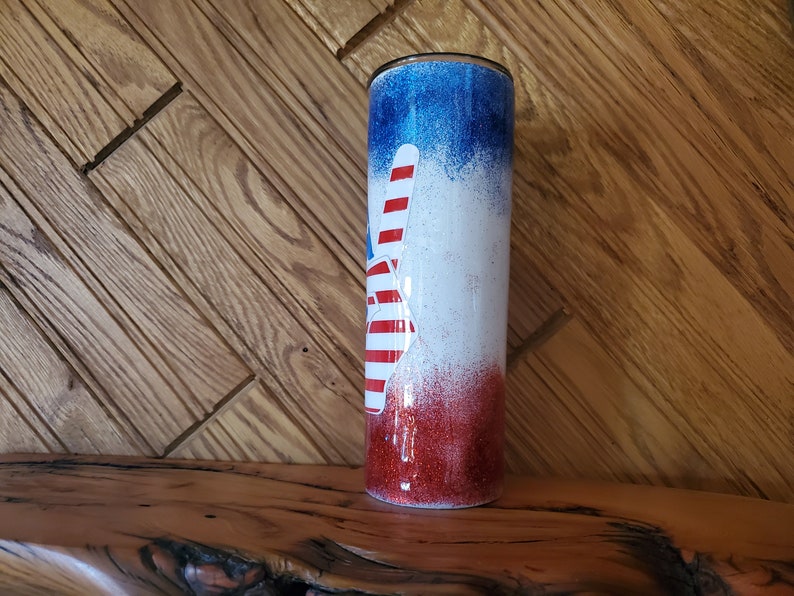 May include: A red, white, and blue glitter tumbler with a peace sign design. The tumbler is made of stainless steel and has a double-wall insulated design.