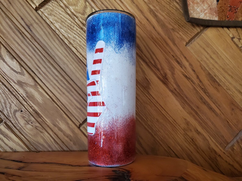 May include: A red, white, and blue glitter tumbler with a peace sign design. The tumbler is made of stainless steel and has a double-walled construction to keep drinks cold or hot for hours.