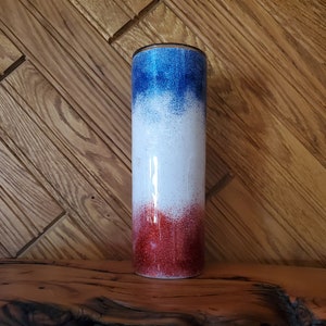 May include: A red, white, and blue ombre glitter tumbler. The tumbler has a stainless steel exterior and a clear lid.