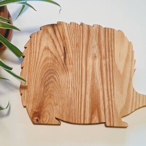 May include: A wooden cutting board shaped like a hedgehog. The board is made of light brown wood with a natural grain pattern.