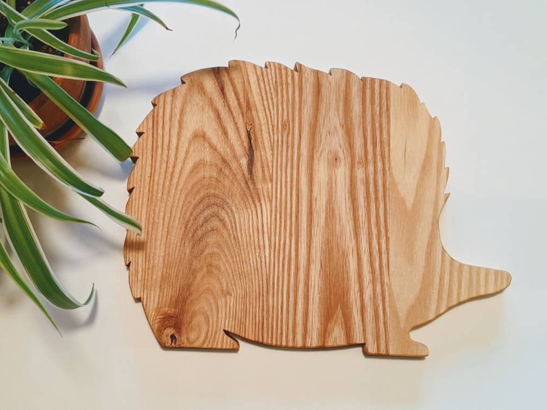 May include: A wooden cutting board shaped like a hedgehog. The board is made of light brown wood with a natural grain pattern.