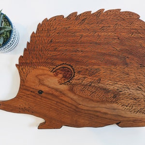 May include: A wooden cutting board shaped like a hedgehog. The board is made of dark wood and has a detailed design of a hedgehog with a brown and black color scheme.
