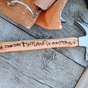 May include: A wooden-handled hammer with a silver head. The handle is engraved with the words "For the dad that can fix anything".