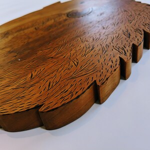 May include: A wooden serving tray with a unique, textured surface that resembles fur. The tray has a brown, natural wood finish and a slightly irregular, wavy edge.