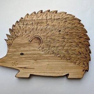 May include: A wooden cutting board shaped like a hedgehog with a detailed burned design. The board is light brown with a natural wood grain.