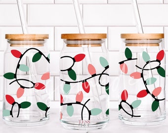 Puede incluir: Tres tarros de vidrio con tapas de madera y pajitas transparentes. Cada tarro tiene un diseño de luces navideñas rojas, verdes y rosas envueltas alrededor del tarro.