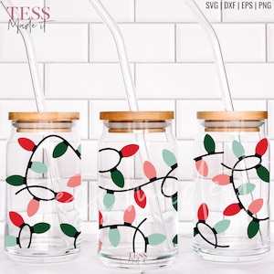 May include: Three glass jars with wooden lids and clear straws. Each jar has a design of red, green, and pink Christmas lights wrapped around the jar.