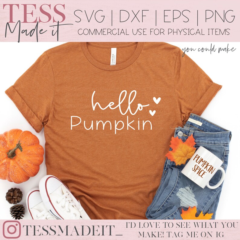 May include: A brown t-shirt with the text "hello pumpkin" in white with two small hearts. The t-shirt is laying on a white surface with a pumpkin, a pair of white sneakers, and a pair of blue jeans with a white mug that says "pumpkin spice".