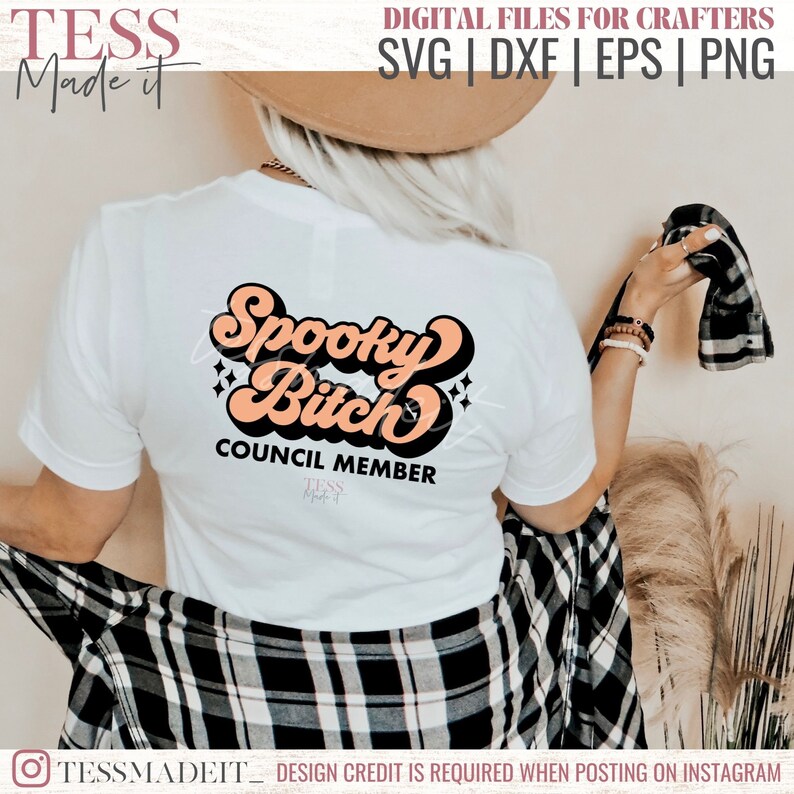 May include: A white t-shirt with a retro-style graphic that says "Spooky Bitch Council Member" in orange and black lettering.