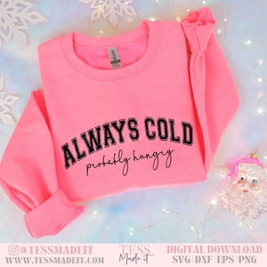 以下が含まれることがあります： ピンクのトレーナーに、黒い文字で「ALWAYS COLD probably hungry」と書かれています。