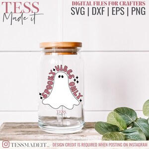 May include: A clear glass tumbler with a wooden lid and a straw. The tumbler has a pink and white design with a ghost and the text "Spooky Vibes Only".