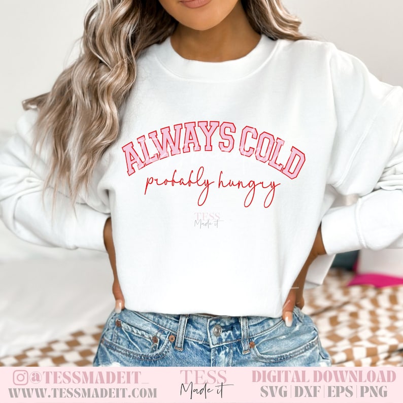 以下が含まれることがあります： 「ALWAYS COLD probably hungry」というピンクと赤の文字が書かれた白いスウェットシャツ。下に「TESS Made it」という小さなロゴがあります。