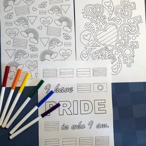 Three coloring pages with various LGBTQIA+ symbols and flags. There are colorful markers at the bottom left of the screen.