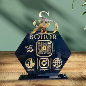 May include: A black hexagonal acrylic stand with gold lettering that reads "Sodor". The stand features a gold QR code, a gold "Scan Here To Pay" arrow, and gold icons for Facebook, Instagram, and a website.