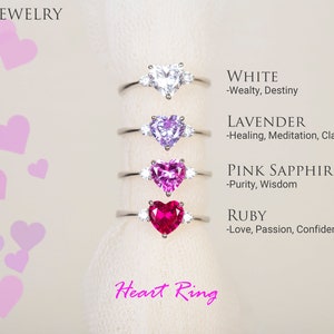 K&ouml;nnte beinhalten: Herzf&ouml;rmige Ringe mit verschiedenen farbigen Edelsteinen, darunter Wei&szlig;, Lavendel, rosa Saphir und Rubin. Jeder Ring hat eine Beschreibung des Edelsteins und seiner Bedeutung, wie "Wei&szlig; - Wohlstand, Schicksal" und "Rubin - Liebe, Leidenschaft, Selbstvertrauen". Die Ringe werden auf einem wei&szlig;en Hintergrund mit rosa Herzen pr&auml;sentiert.