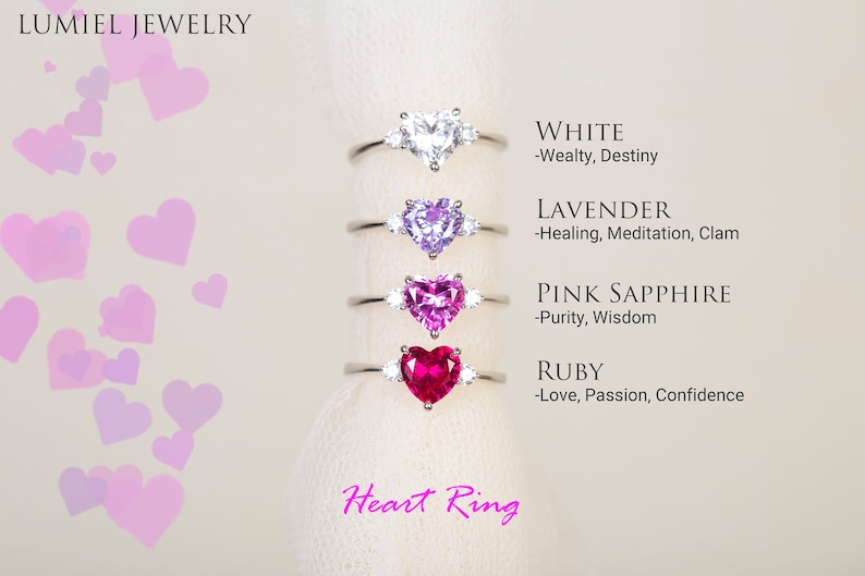 K&ouml;nnte beinhalten: Herzf&ouml;rmige Ringe mit verschiedenen farbigen Edelsteinen, darunter Wei&szlig;, Lavendel, rosa Saphir und Rubin. Jeder Ring hat eine Beschreibung des Edelsteins und seiner Bedeutung, wie "Wei&szlig; - Wohlstand, Schicksal" und "Rubin - Liebe, Leidenschaft, Selbstvertrauen". Die Ringe werden auf einem wei&szlig;en Hintergrund mit rosa Herzen pr&auml;sentiert.