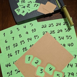 May include: Green and brown paper squares with numbers written on them. The numbers range from 1 to 40. There are also five smaller green squares with the numbers 1 through 5 written on them.