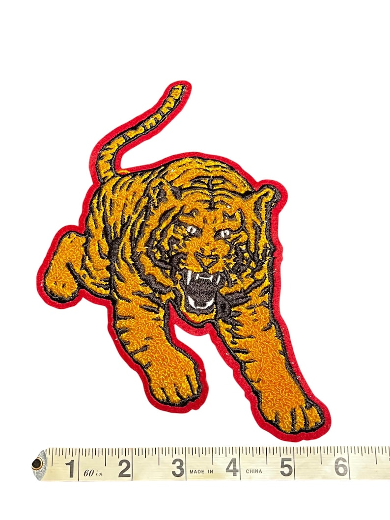 May include: Embroidered tiger patch in shades of gold and black, outlined in red. The tiger is depicted in a running pose with an open mouth, showcasing its teeth. The patch is approximately 5 inches in length.