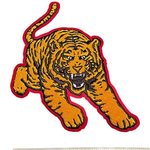 May include: Embroidered tiger patch in shades of orange and black, outlined with a red border. The tiger is depicted in a dynamic pose with its mouth open, showcasing its teeth. The patch is designed for application on clothing or accessories.