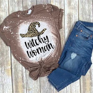 May include: A brown t-shirt with a bleach-splattered design featuring a black and brown witch hat and the text "Witchy Woman".