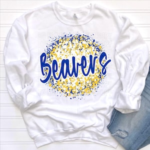 May include: White sweatshirt with the word "Beavers" in blue script, surrounded by a blue and yellow speckled design. The sweatshirt is paired with blue jeans.