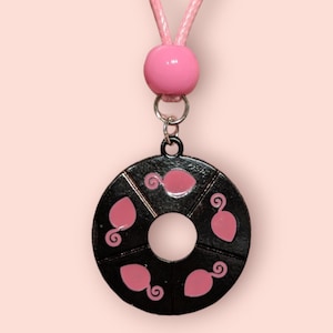 May include: A black metal necklace with a pink bead and a round pendant featuring five pink ladybug silhouettes.