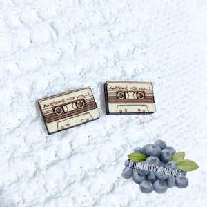 May include: A pair of wooden earrings shaped like cassette tapes. The tapes are labeled "Awesome Mix Vol. 1".