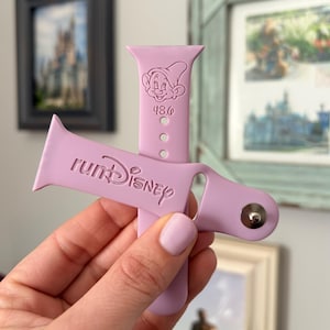 May include: A lilac watch strap featuring the text "runDisney" and a cartoon image of Dopey. The strap has three adjustment holes and a silver clasp. The number "48.6" is printed below the Dopey image.