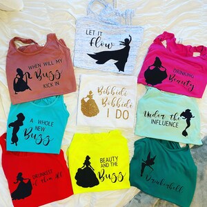 May include: Ten different tank tops with various Disney character silhouettes and text. The text includes "When will my Buzz kick in", "A whole new Buzz", "Let it flow", "Bibbidi Bobbidi I do", "Drinking Beauty", "Under the influence", "Drunkest of them all", "Beauty and the Buzz", and "Drinkerbell".