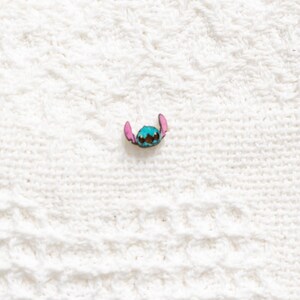 May include: A blue and pink Stitch character pin. The pin is made of metal and has a shiny finish.