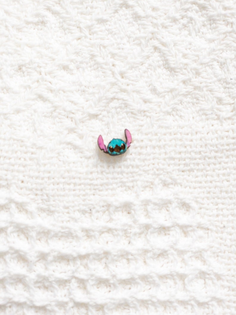May include: A blue and pink Stitch character pin. The pin is made of metal and has a shiny finish.