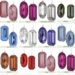 Puede incluir: Una colección de adornos colgantes con forma de gema facetada en varios colores, incluyendo rosa, fucsia, champán, esmeralda, zafiro, transparente, morado, azul claro, cobre y rojo. Cada adorno cuenta con un lazo metálico para colgar.