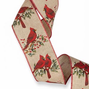 May include: A tan-colored wired ribbon featuring a repeating pattern of bright red cardinal birds perched on green pine branches with small red berries. The edges of the ribbon are finished with a stitched red thread border.