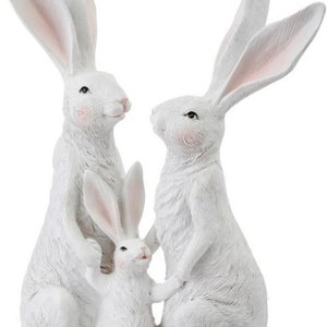 May include: A white rabbit family figurine set. The set includes two adult rabbits and one baby rabbit. The rabbits are standing upright with their ears perked up. The baby rabbit is standing between the two adult rabbits.