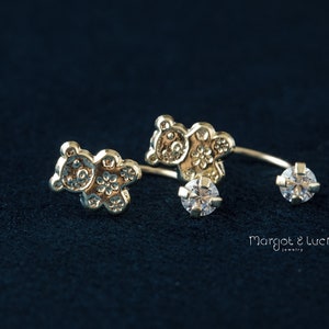 May include: A pair of gold-toned bear-shaped earrings with a clear crystal on each earring. The earrings are designed to be worn on the upper ear.