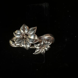 May include: A silver ring with two flower designs. The flowers are detailed and have a textured finish.