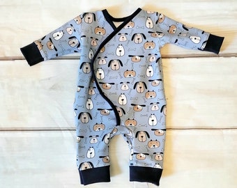 Puede incluir: Un pelele azul para bebé con un patrón de perros y huesos. El pelele tiene ribetes negros alrededor del cuello, las mangas y las piernas.