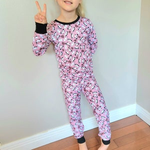 May include: Pink pajamas with a black and white milk carton and panda print. The pajamas have long sleeves and long pants.