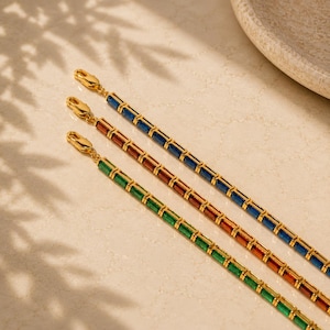 May include: Three gold-toned chain bracelets featuring rectangular-cut gemstones in blue, amber, and green. Each bracelet is constructed with a series of linked settings and finished with a gold-toned lobster claw clasp at the end of the chain.