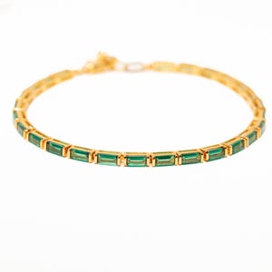 Könnte beinhalten: Ein goldenes Armband mit einer Reihe von smaragdgrünen Baguette-Steinen.