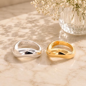May include: Two rings with a smooth, organic, irregular shape. One ring is polished silver and the other is polished gold. Both rings feature a 925 hallmark stamped on the inner band, indicating sterling silver composition for both pieces.