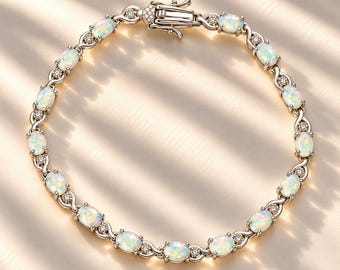 Könnte beinhalten: Ein silberfarbenes Armband mit einer Reihe ovaler, irisierender Opale, die sich mit kleinen runden, klaren Steinen abwechseln. Die Glieder sind durch ein feines Metallmuster verbunden und das Schmuckstück wird mit einem rechteckigen Kastenverschluss geschlossen.