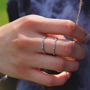 Könnte beinhalten: Zwei dünne Silberringe mit einem Regenbogen aus kleinen Edelsteinen, die in einer durchgehenden Linie um das Band gelegt sind.