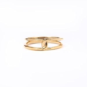 May include: A gold ring with a double band design. The bands are connected by a knot in the center.