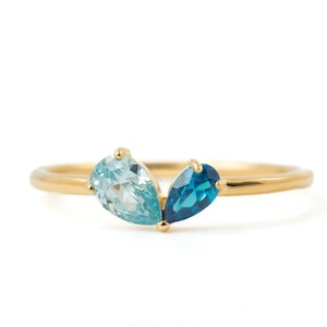 May include: A gold ring featuring two pear-shaped gemstones, one light blue and one dark blue. The gemstones are set side-by-side, creating a unique and elegant design. The ring's band is a simple, polished gold.