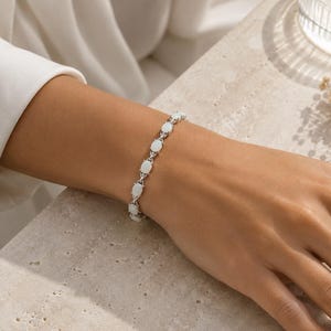 May include: A silver-toned link bracelet featuring a series of oval-shaped, iridescent white opal stones. Each stone is set within a metallic frame, connected by small, polished silver links that create a continuous, flexible chain design.