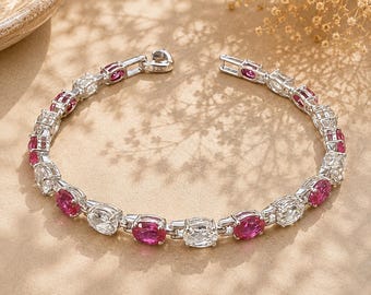May include: A silver-toned bracelet featuring alternating oval-cut deep pink gemstones and clear white stones set in a linked chain. The clasp mechanism is clearly visible and stamped with 925, indicating sterling silver construction.