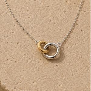 May include: A delicate necklace featuring a thin silver chain connected to two interlocking circular rings. One ring is finished in a polished gold tone, while the other ring is finished in a polished silver tone, creating a two-tone metal design.